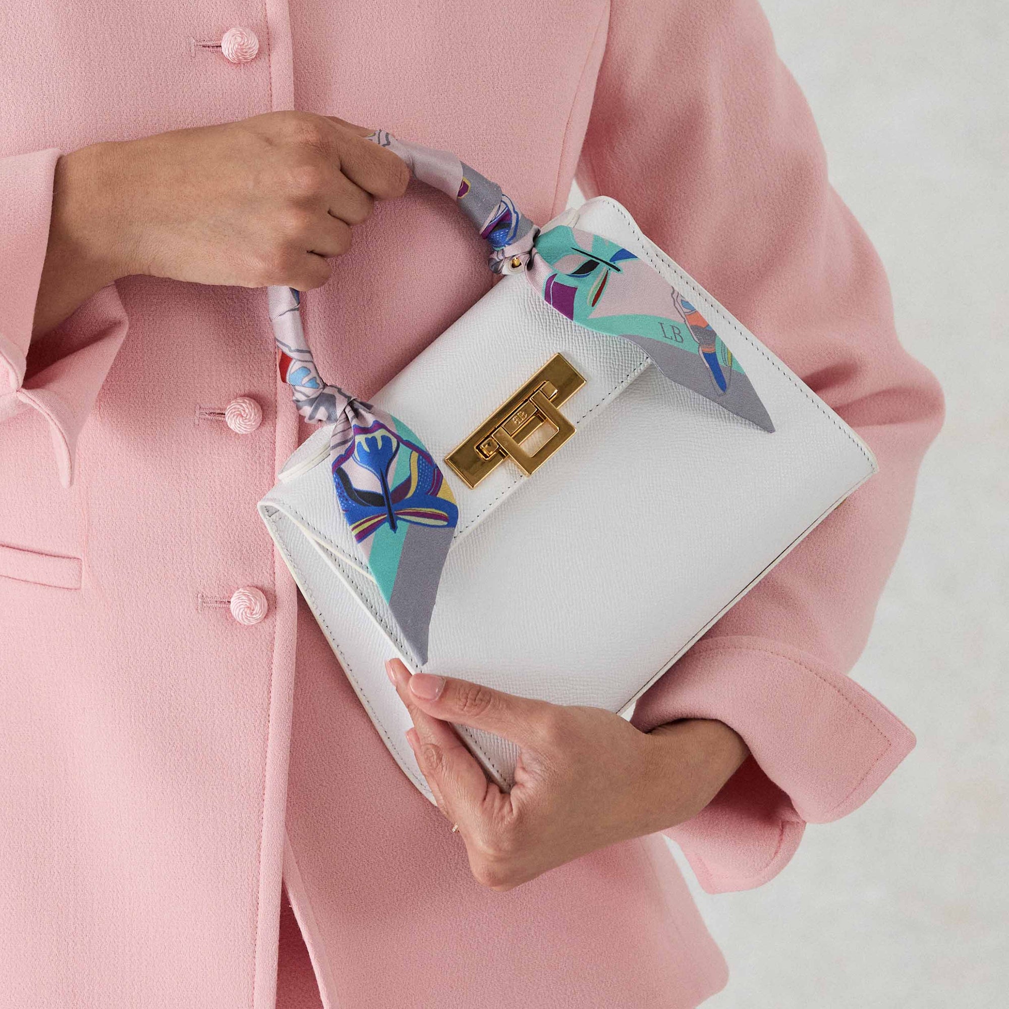 White Fonteyn handbag with floral silk scarf wrapped held by a person wearing a pink coat.