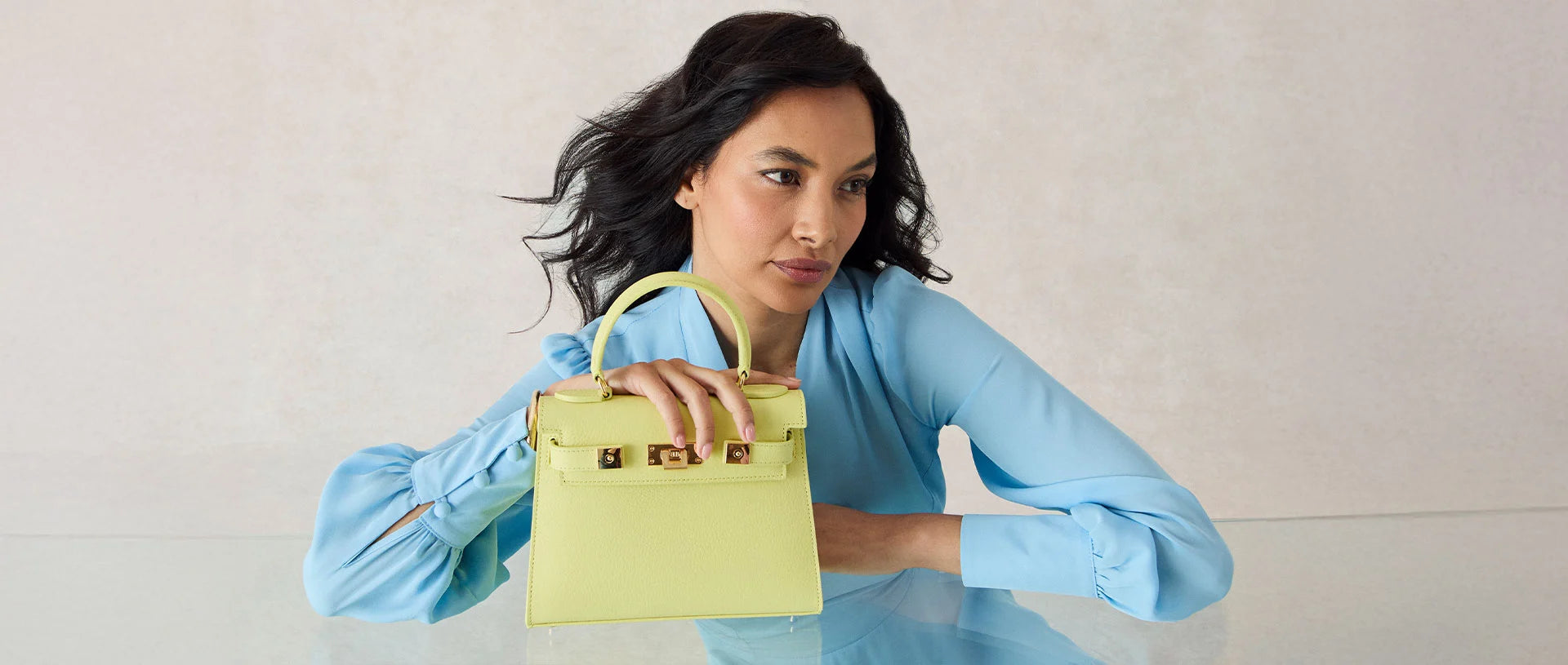 Woman holding a Primose coloured Maya Midi handbag against a neutral background.