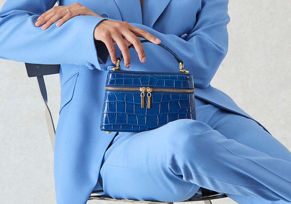 Person wearing a blue suit holding a matching blue Lalage Beaumont Ninette handbag
