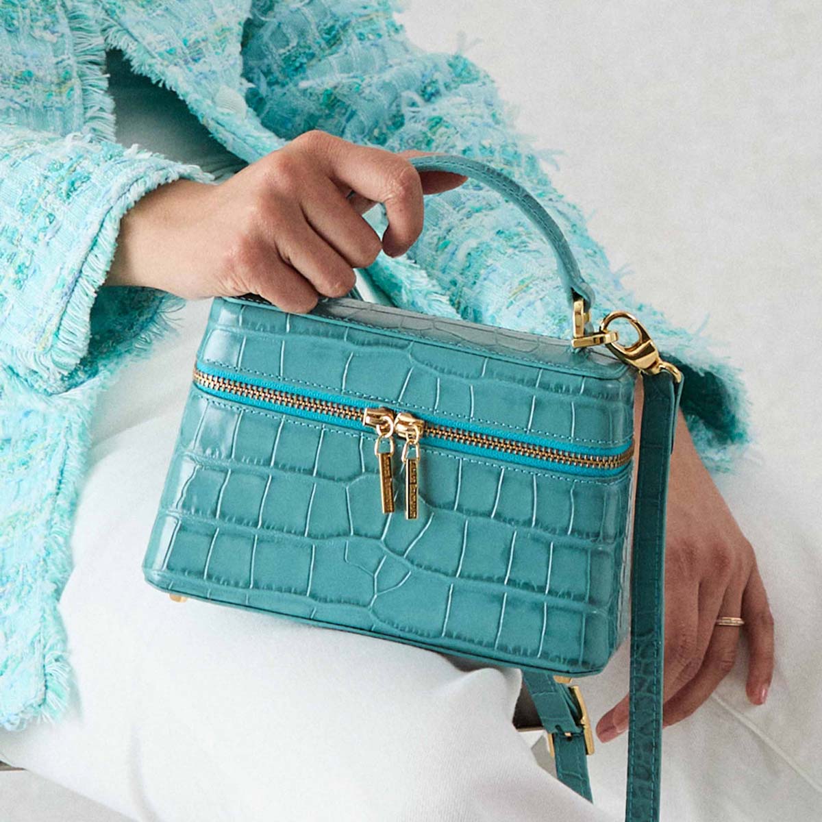 Turquoise Ninette handbag with gold accents held by a person wearing a matching turquoise jacket.