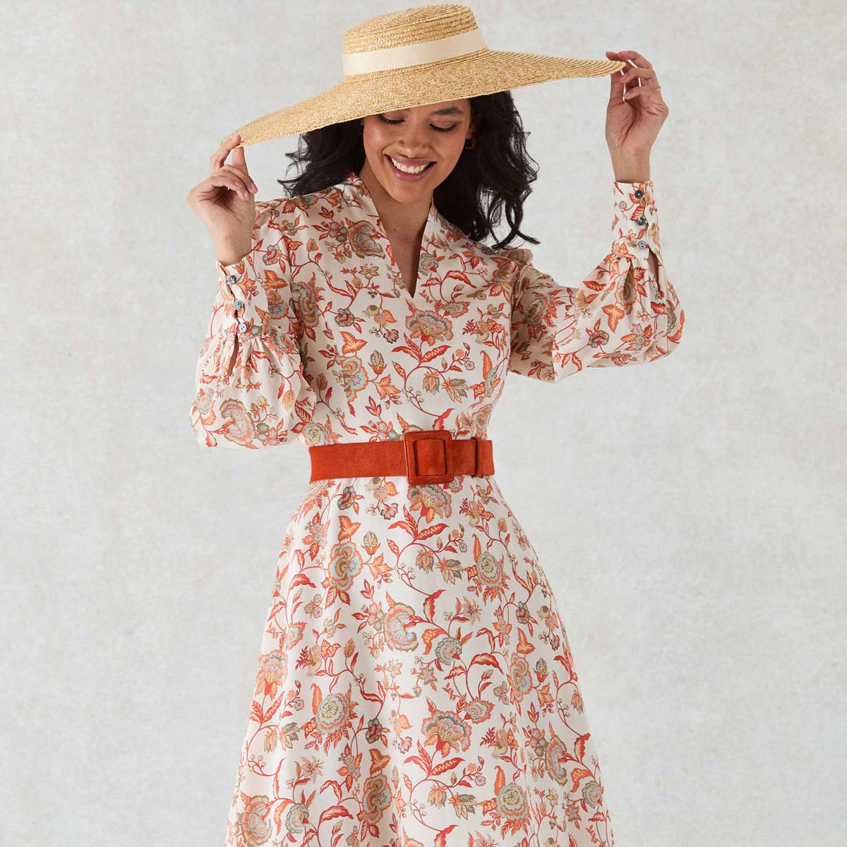 Woman wearing a floral dress with a wide-brimmed hat against a plain background