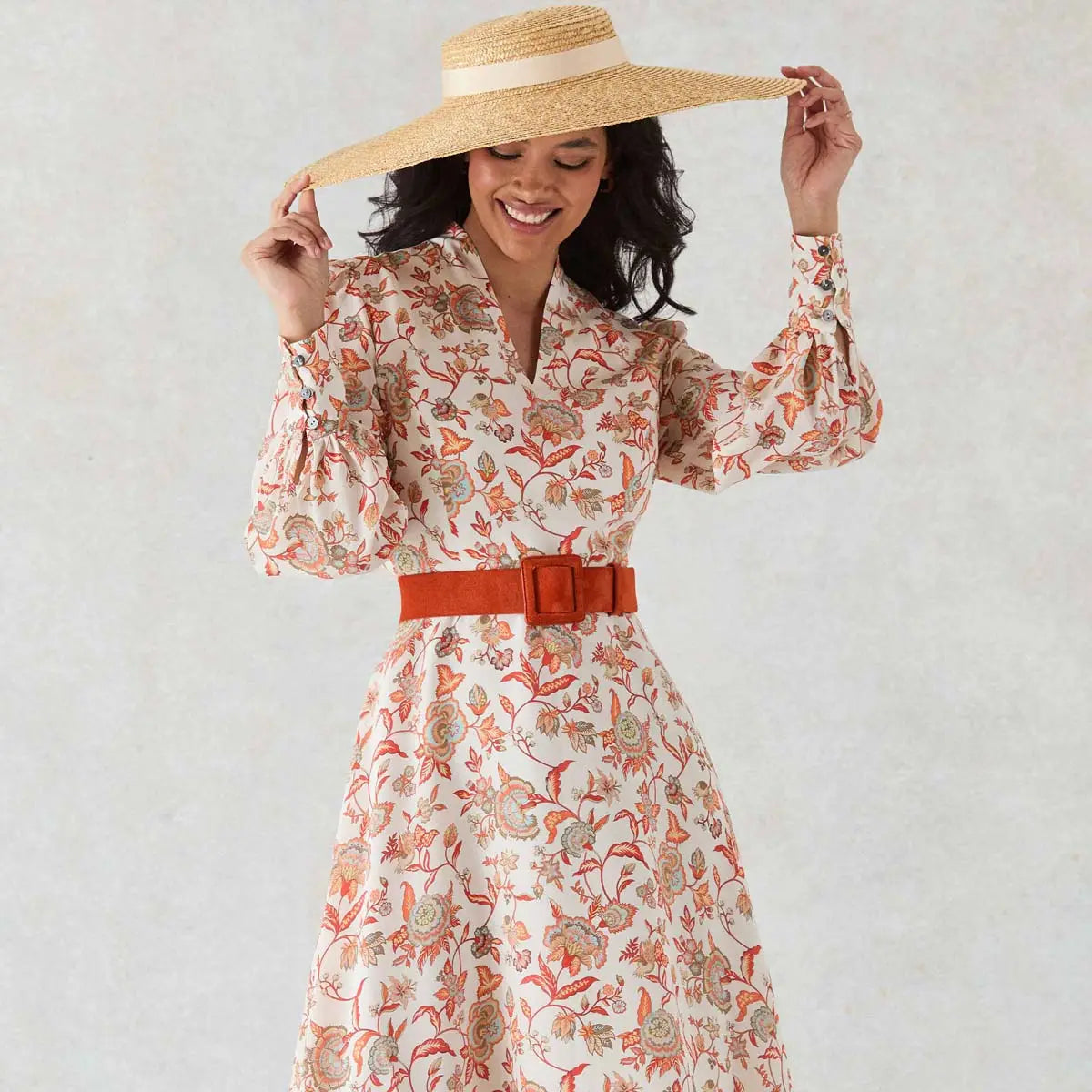 Woman wearing a floral dress with a wide-brimmed hat against a plain 