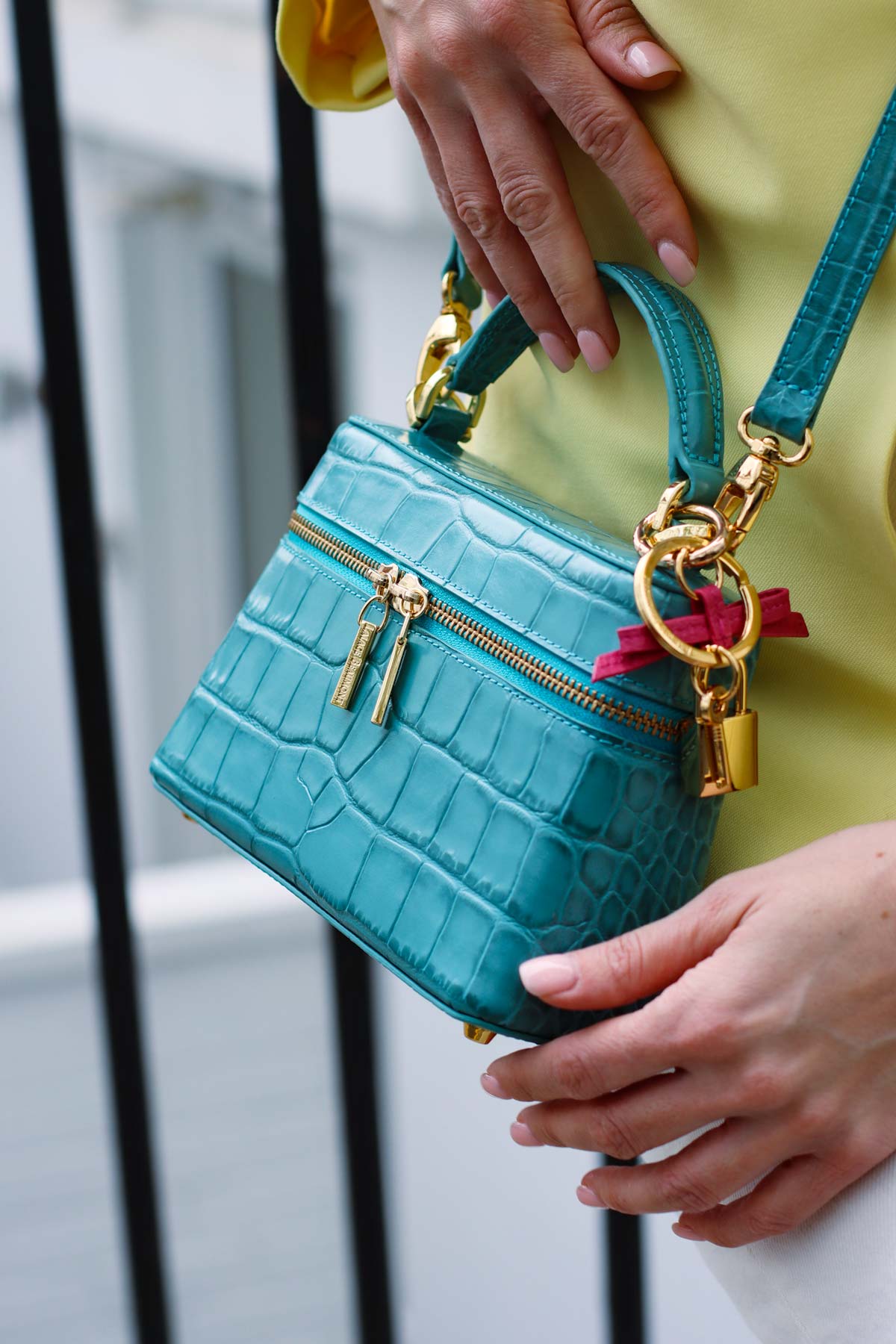 Lalage Beaumont ninette orinoco Topaz handbag with gold accents held by a person against a blurred background