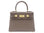 A taupe colored, medium-sized handbag made from grainy print Italian calf leather, featuring gold-plated hardware and a top handle with a detachable shoulder strap.