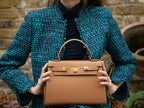 Woman holding a large tan pebble print Italian calf leather handbag with top handle, detachable strap and gold plated hardware